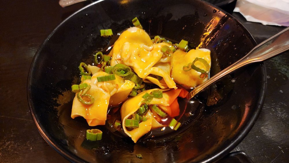 Wontons in chili oil with scallions in a black bowl