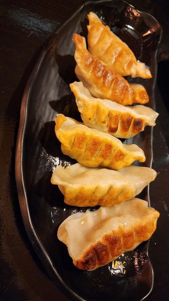 Six pan-fried dumplings on a black plate