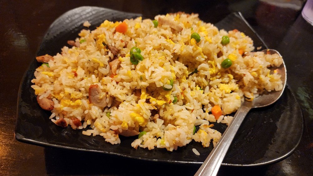 Fried rice with egg, peas and carrot on a black plate